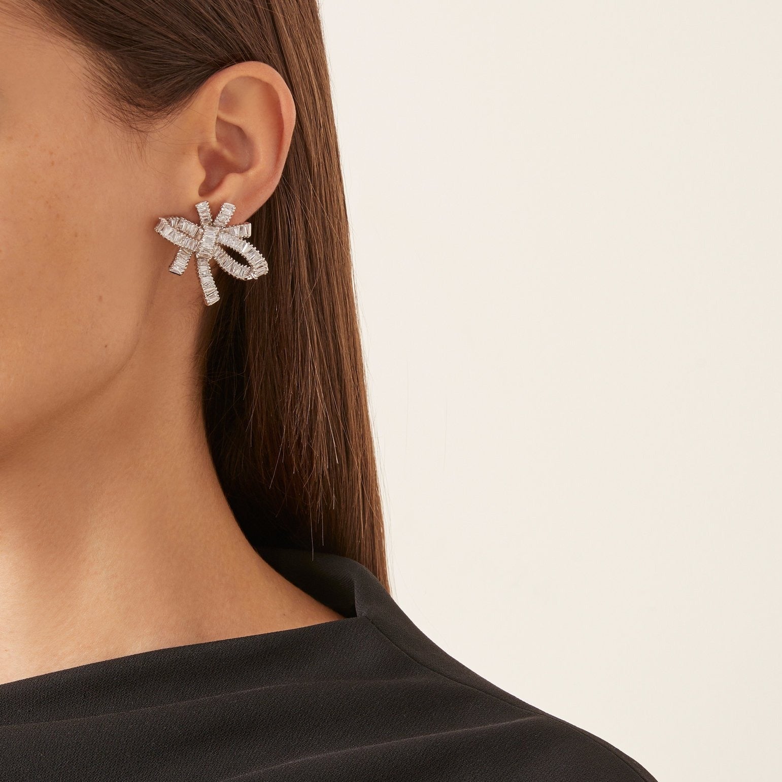 THE FALLON BAGUETTE BOW CLUSTER EARRINGS IN RHODIUM. Statement bow earrings made from plated brass and cubic zirconia.